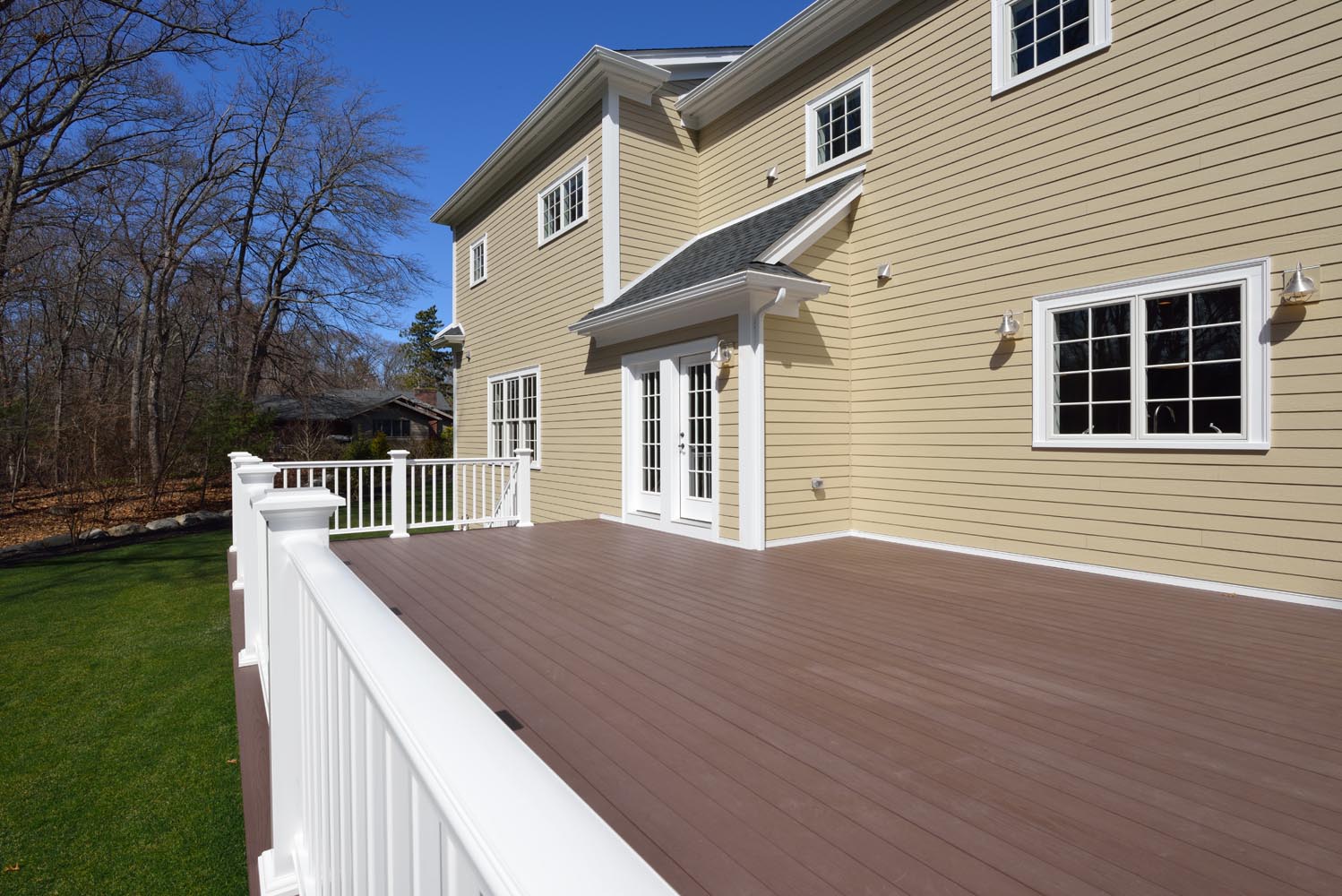 Large new deck in house backyard. Composite boards, white railing posts and veranda