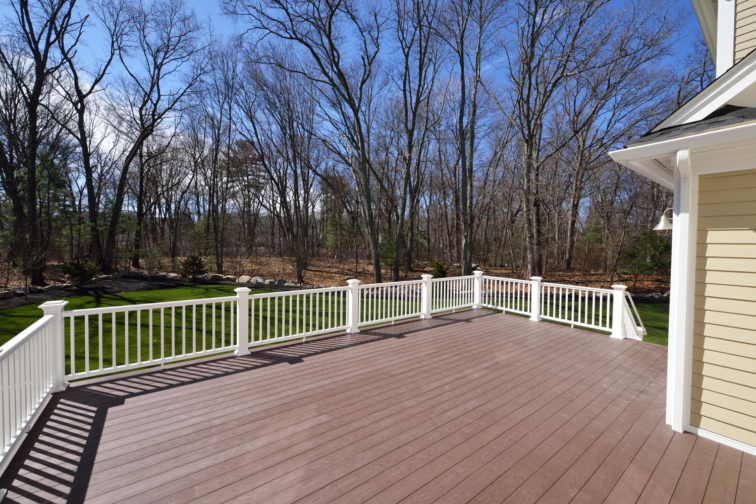 New backyard deck. White vinyl railings and composite brown boards. Large patio and garden space with a view to the woods.